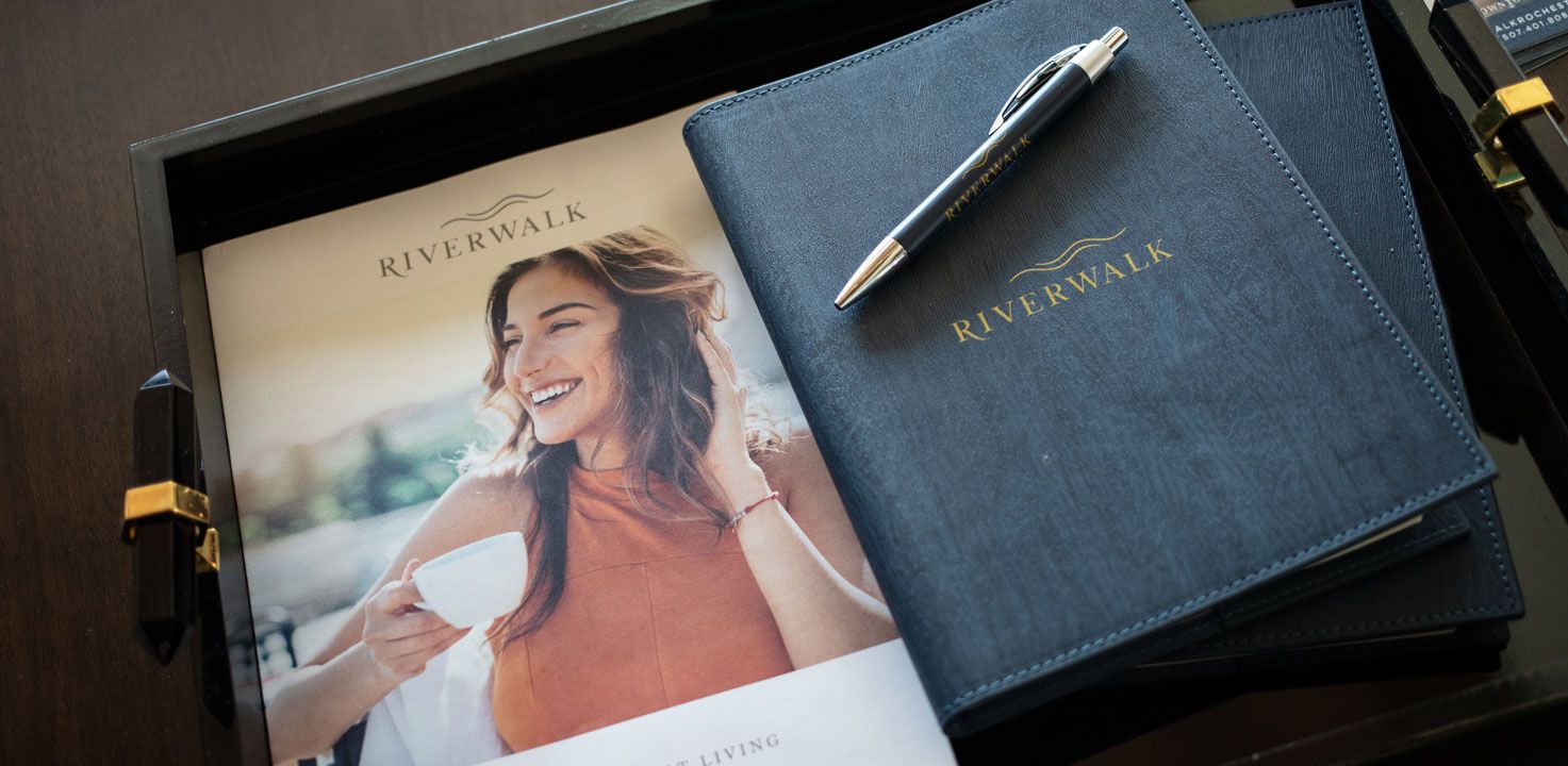 A Riverwalk brochure and leasing folder with a pen