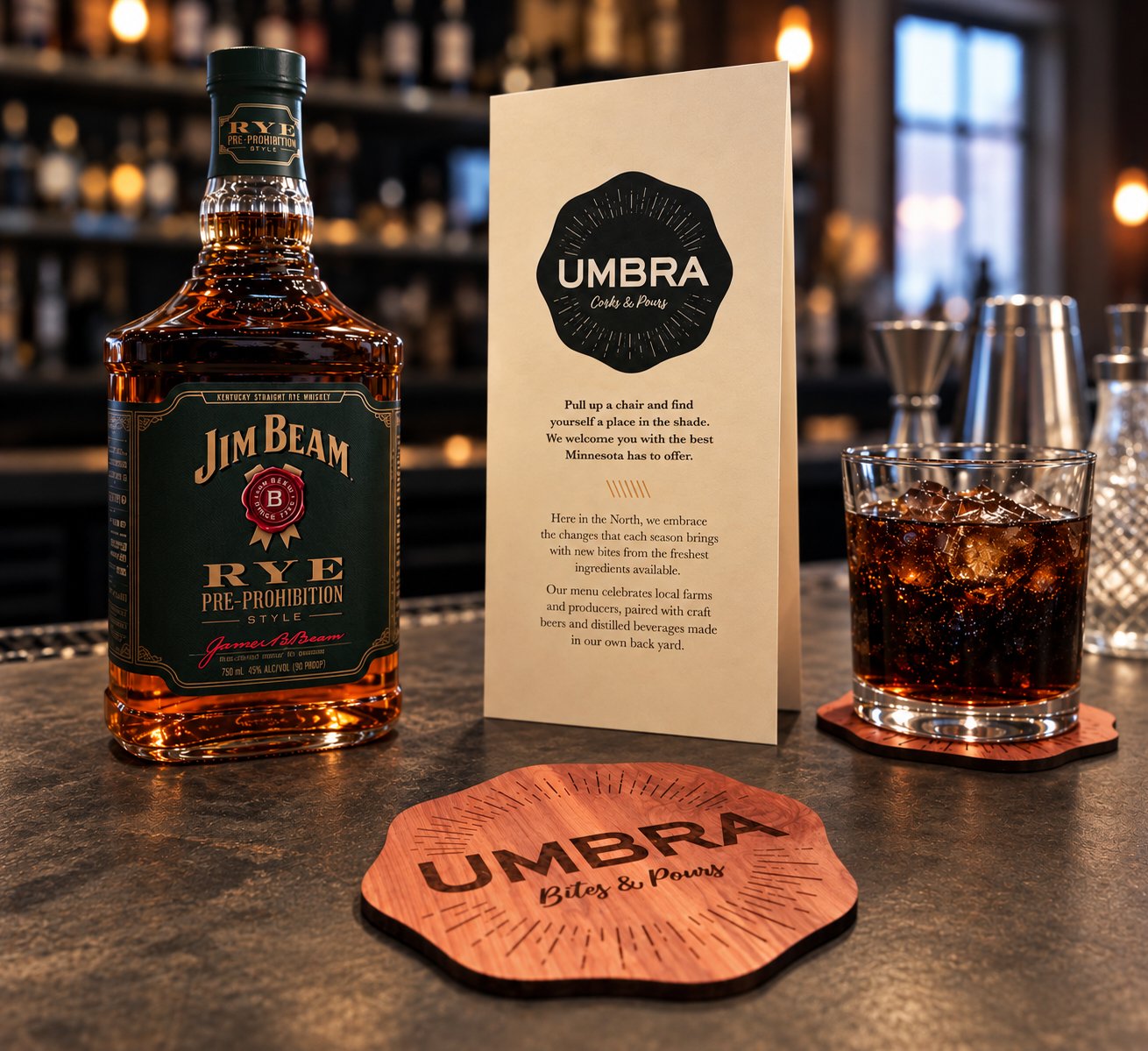 An Umbra coaster and bar card on the bar, beside a bottle of rye and a drink