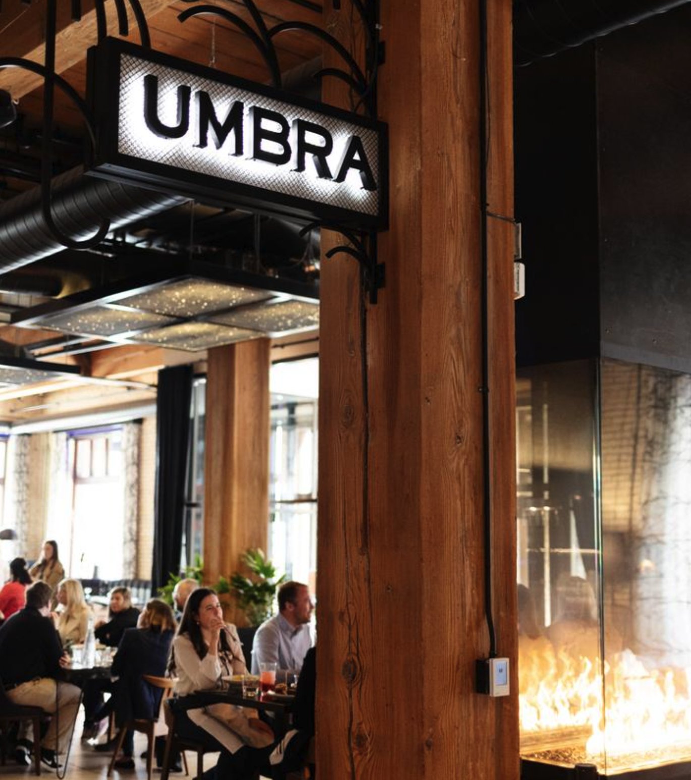 The lit Umbra sign hanging over the dining room, with guests at their tables