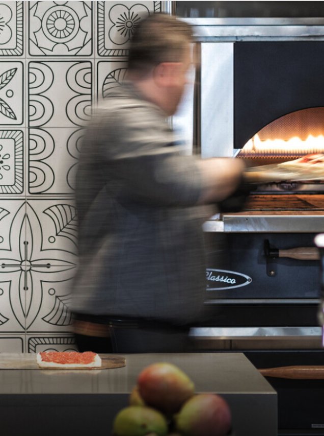 A cook at the pizza oven in front of Umbra’s patterned tile wall