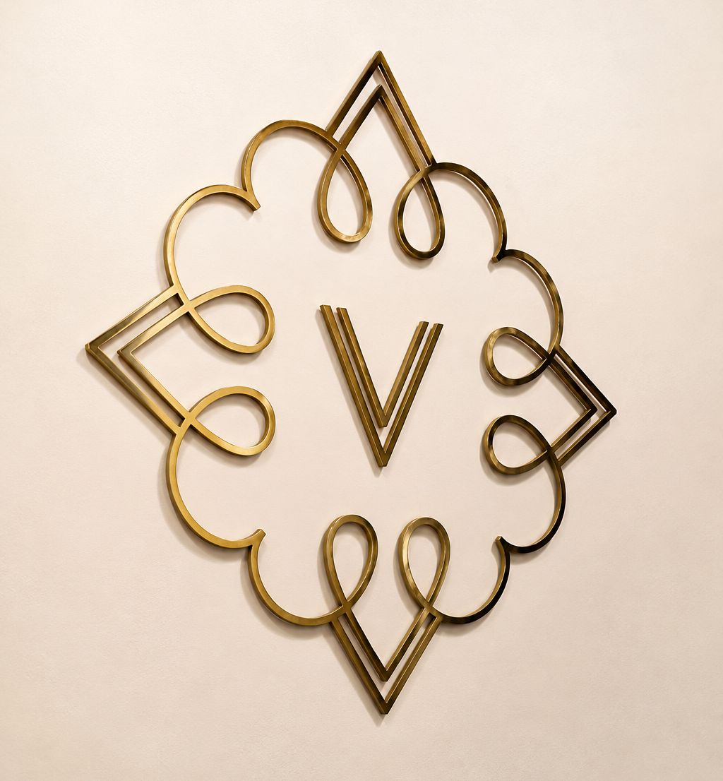 The Vicinity V logo in gold on a cream wall